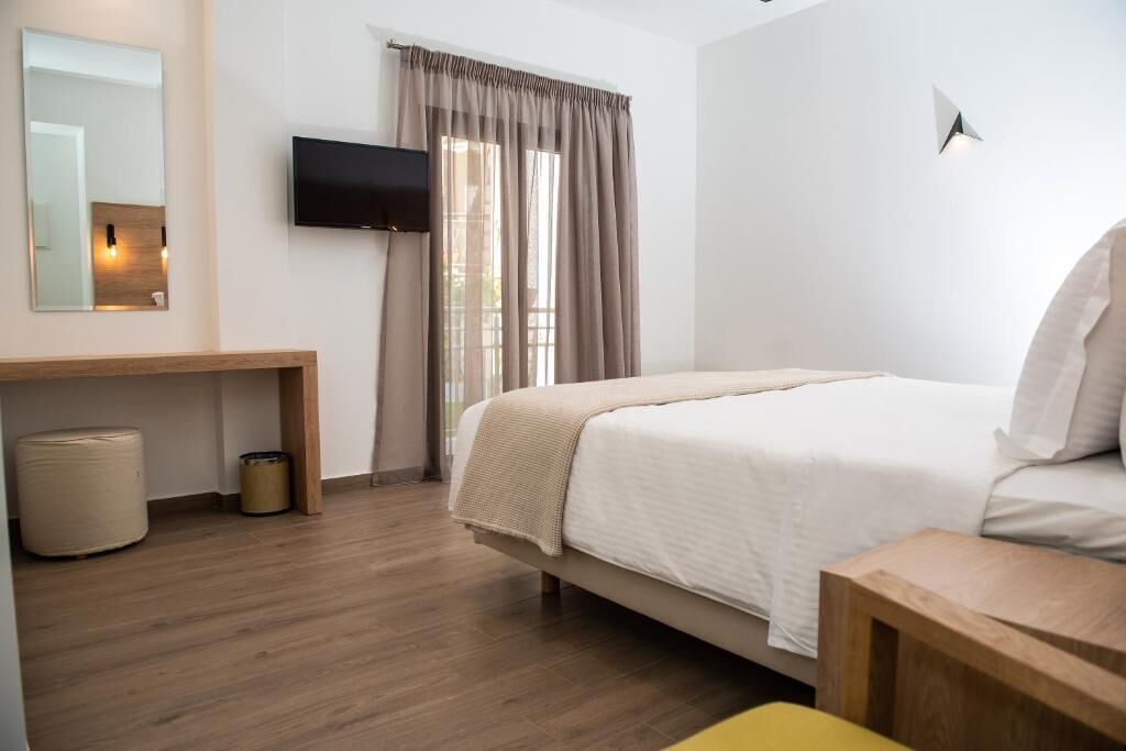 A hotel room with a bed, a TV mounted on the wall, a wooden bench, and a window with curtains.
