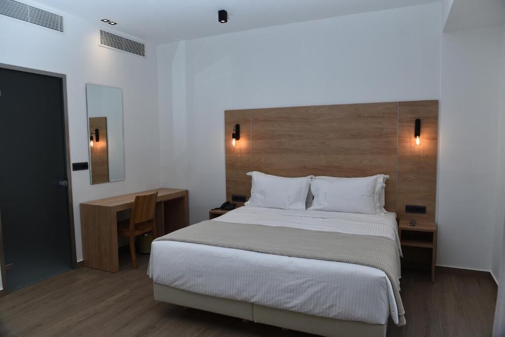A modern hotel room with a large bed, a wooden headboard, bedside tables, a desk, and a mirror.