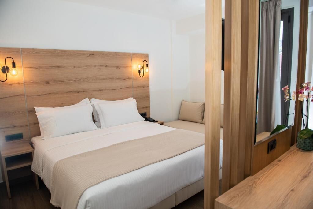 Une chambre d’hôtel avec une tête de lit en bois, un lit avec du linge de lit blanc, une table de chevet et une table en bois.