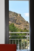 Vista desde un balcón con barandilla, que domina una colina rocosa con una estructura similar a una fortaleza.