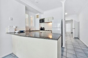 Kitchen features a central island with a microwave and oven, white cabinetry, and grey countertop.