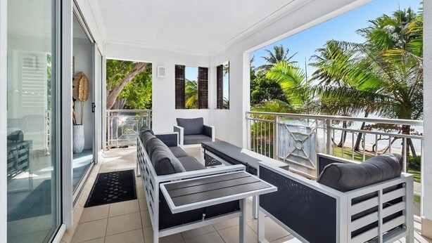 A balcony with a sofa, a table, and a chair. There is a glass door leading to the interior. - 1 Bedroom Apartment 301/1 in Alassio Resort (Palm Cove)