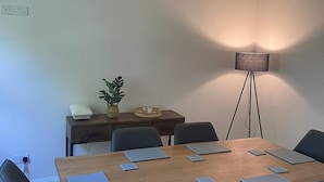 Een vergaderruimte met een houten tafel, zes stoelen, een vloerlamp en een potplant.