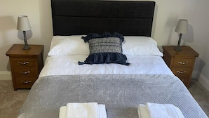 Een net opgemaakt bed met witte lakens, een donker hoofdbord en twee bedlampjes.