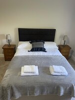 A neatly made bed with white linens, a dark headboard, and two bedside lamps.