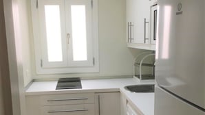 A compact kitchen with a built-in washing machine, a sink, and a window with blinds. - Cozy Studio in Marbella Old Town, Steps from Beach & Historic Sights (Marbella)