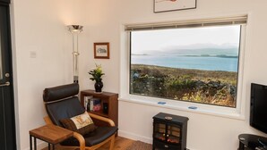 A cozy living room with a large window overlooking a scenic landscape, a comfortable leather chair, a small wooden table, and a decorative vase.