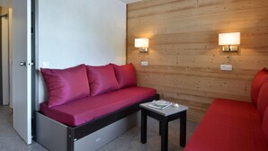 A compact room with a sofa, a small table, and two wall-mounted lights. - Renovated Divisible Studio at the Foot of the Slopes with Balcony and Pets Allowed (Plagne Bellecôte)