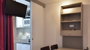 A compact kitchen with a microwave, a dishwasher, and a small cabinet. There is a dining table with chairs and a TV mounted on the wall. - Renovated Divisible Studio at the Foot of the Slopes with Balcony and Pets Allowed (Plagne Bellecôte)