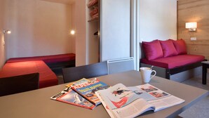 A modern room with a bed, a table with magazines, and a red sofa. - Renovated Divisible Studio at the Foot of the Slopes with Balcony and Pets Allowed (Plagne Bellecôte)