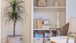 A room with a white bookshelf, a wicker basket, a potted plant, and a wicker chair. - Outrigger @ Boomerang Beach (Boomerang Beach)