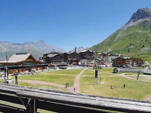 A mountain resort with a large building labeled "MAISON DE TIGNES" and several smaller structures, surrounded by green hills and mountains.