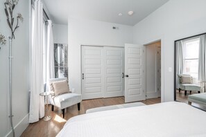 A bedroom with a large bed, a chair, a small table, and a wardrobe. - Rhapsody in Blue | OTR (Cincinnati)