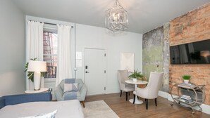 Une chambre moderne avec un grand lit, un bureau, deux chaises, une petite table, une bibliothèque et un mur décoratif en briques.