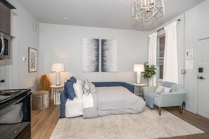 A bedroom with a bed, bedside tables, a lamp, a chair, a plant, and artwork on the wall.
