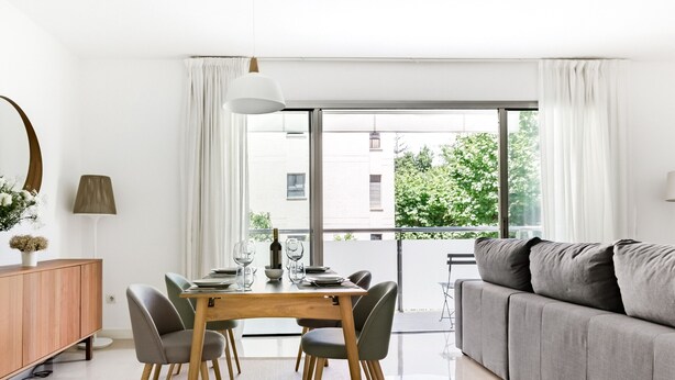 Un salon moderne avec un canapé et un coin repas, de grandes fenêtres et une vue sur la verdure environnante.
