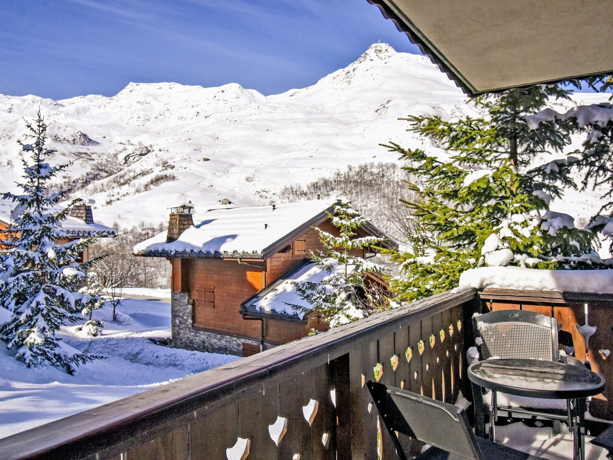 A wooden balcony with a view of a snow-covered mountain and a wooden cabin.