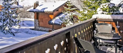 Een houten balkon met uitzicht op een met sneeuw bedekte berg en een houten hut.