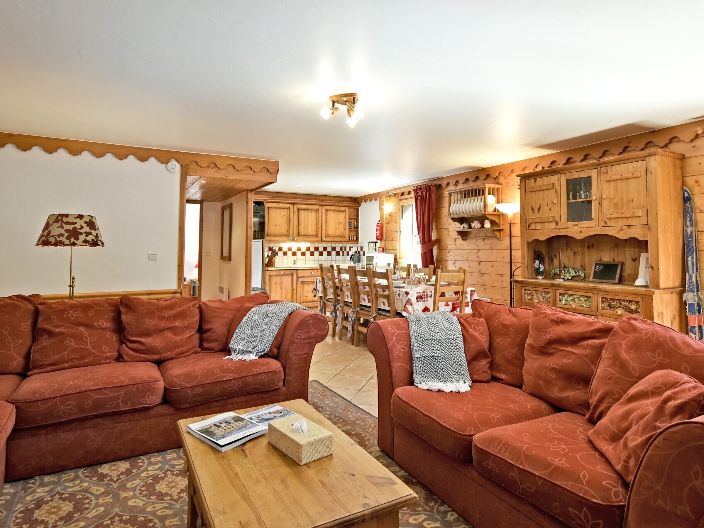 A cozy living room with two sofas, a coffee table with magazines, and a kitchen in the background.