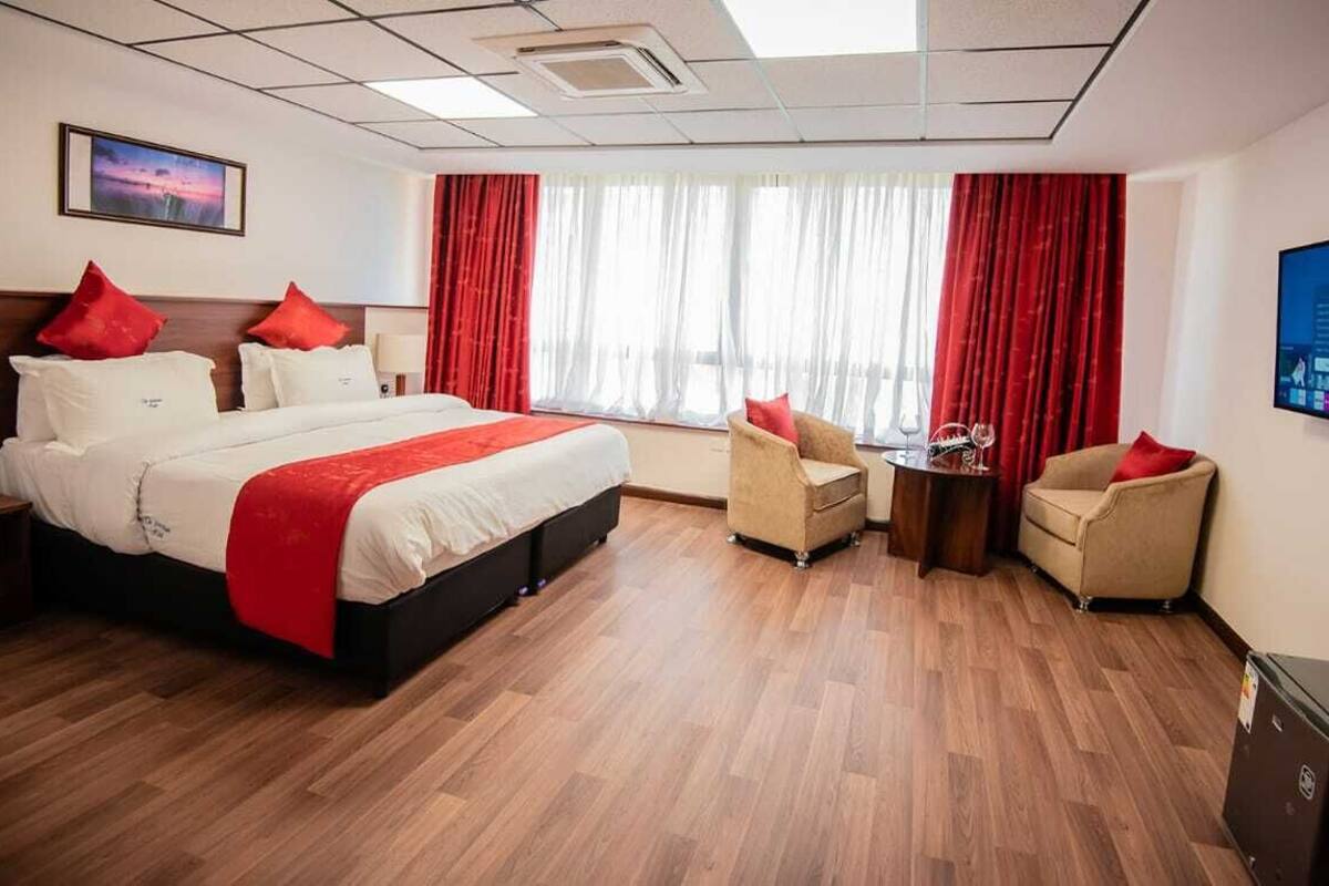 Una habitación de hotel con una cama grande, dos sillones, una mesita y un televisor en la pared.