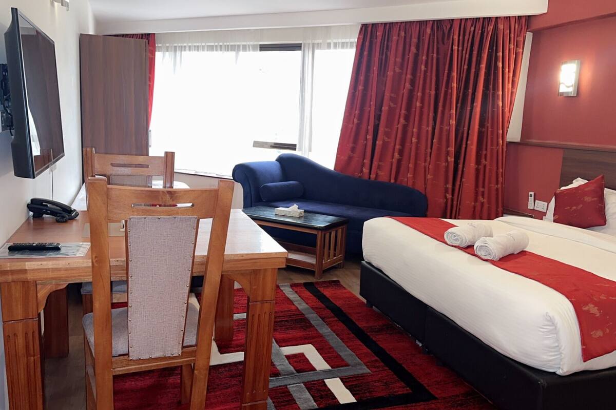 Una habitación de hotel con cama, sofá, escritorio y teléfono, y una televisión.