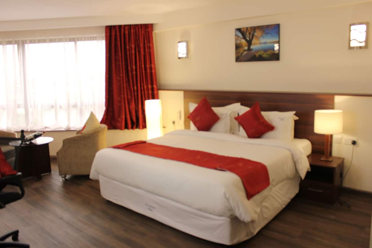 Habitación de hotel con una cama grande, un escritorio, una silla y una mesita de noche con lámpara.