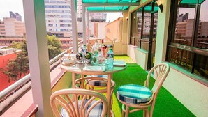 Een balkon met kunstgras, rieten stoelen en een tafel met glazen en flessen.