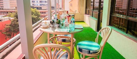A balcony with artificial grass, wicker chairs, and a table set with glasses and bottles.