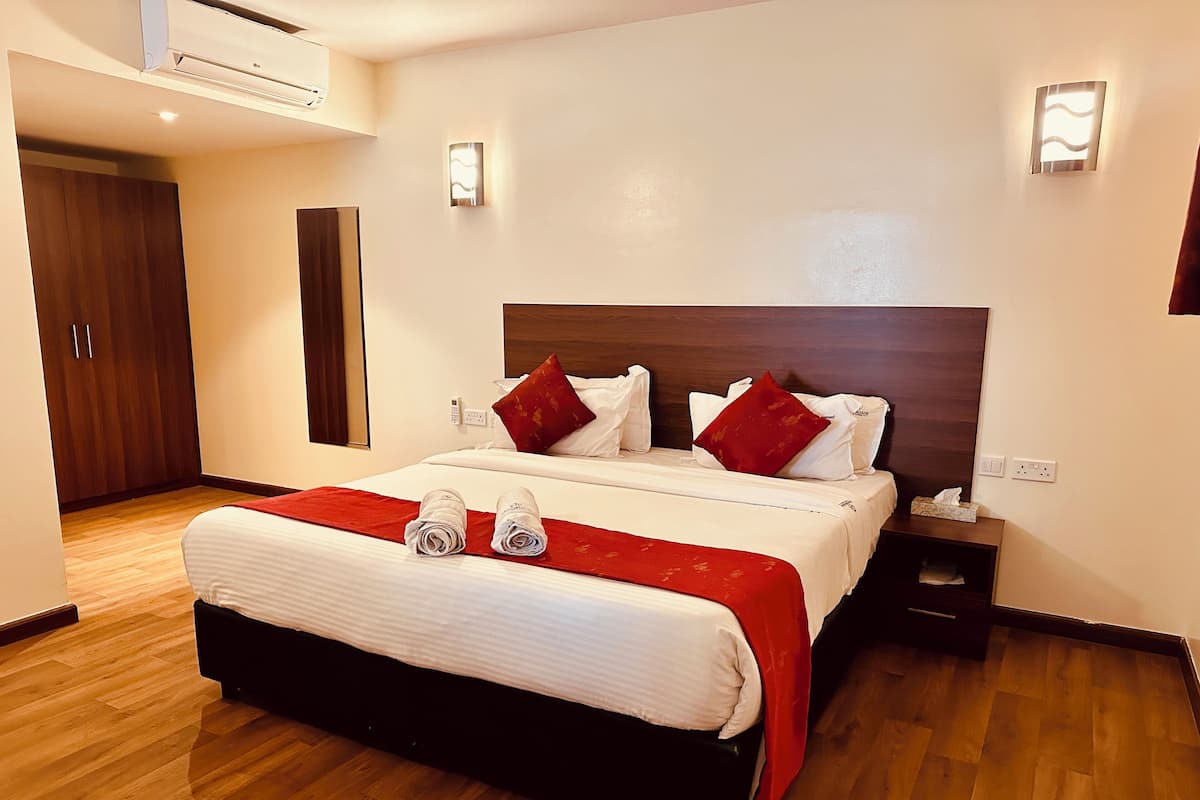 Una habitación de hotel con una cama grande, dos mesitas de noche, un armario y aire acondicionado instalado en la pared.