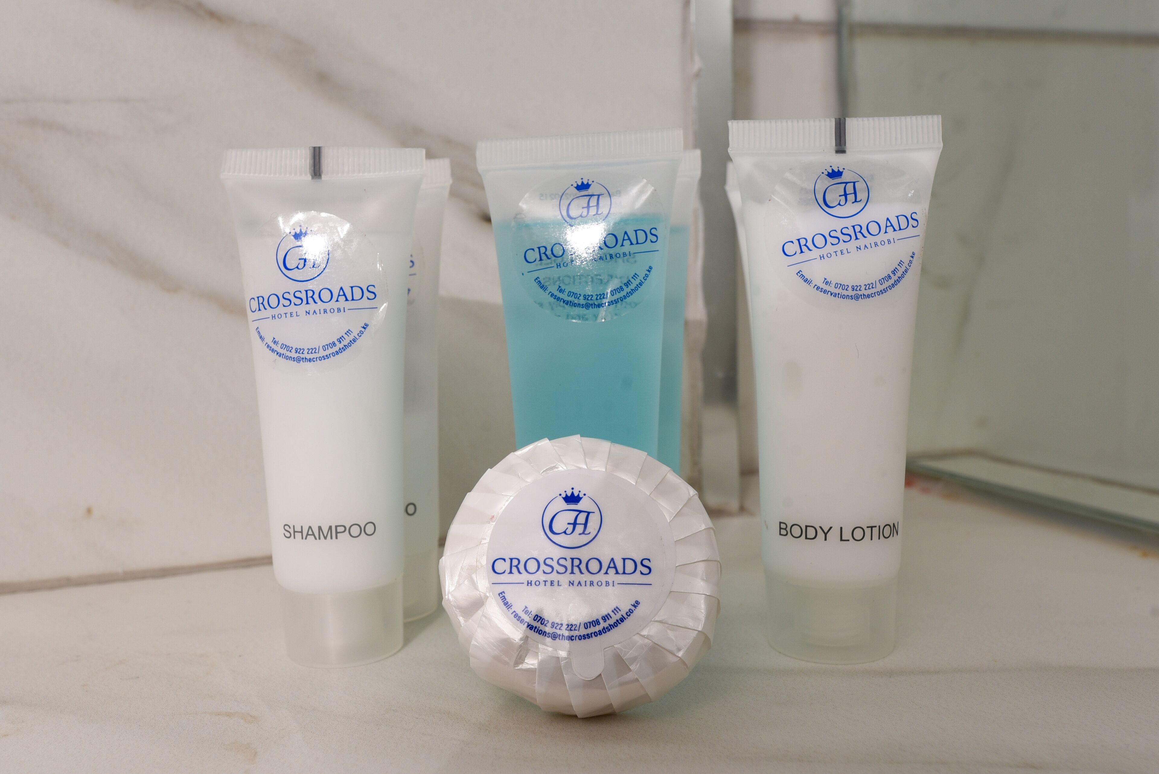 Drei Produkte des Crossroads Hotel Nairobi: Shampoo, Körperlotion und eine blaue Flüssigkeit.