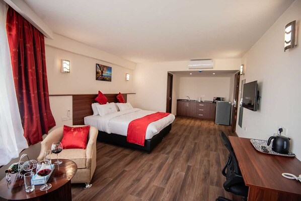 Habitación de hotel con cama, escritorio, silla, una mesita con copas de vino y una kitchenette.