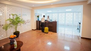Een hotel receptie met een receptioniste, een gast met een koffer en een decoratieve plant.