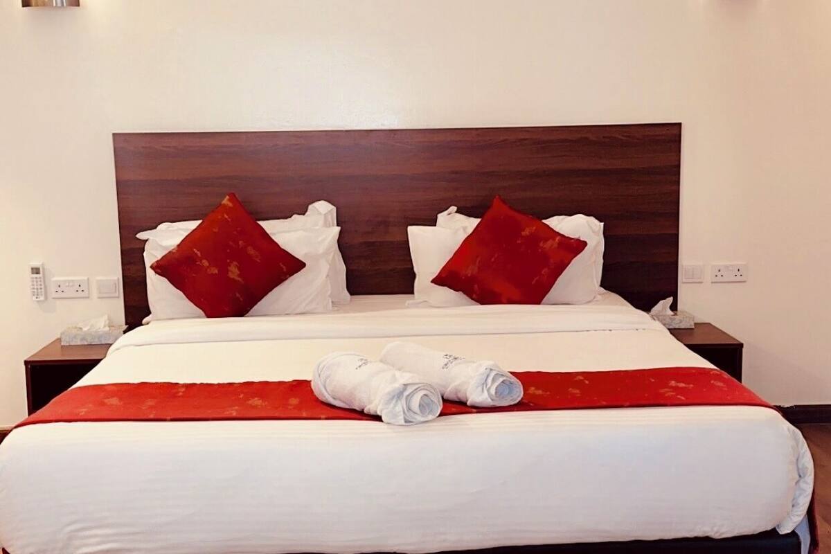 Habitación de hotel con una cama grande, cabecera de madera, dos mesitas de noche y dos lámparas fijadas a la pared.