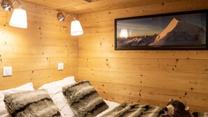 Ein gemütlicher Holzraum mit einem Bett, einem gerahmten Bild einer Berglandschaft und einem Teddybär auf dem Bett.