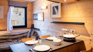 Ein gemütliches Holzhaus-Interieur mit einem Esstisch für zwei Personen, einem Fellüberwurf und gerahmten Bildern an der Wand.