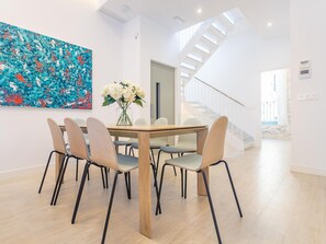 A modern dining area with a wooden table and six chairs, a large abstract painting on the wall, and a staircase leading to an upper level. - Charming 6-Bedroom House with Terraces in the Heart of Historic Seville (Sevilla)