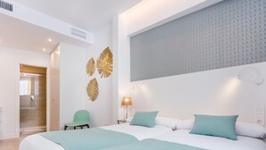 Camera d'albergo con due letti, una sedia, una lampada e un pannello decorativo a parete.