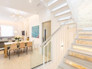 Una sala de estar moderna con comedor, una escalera y un ventanal amplio.