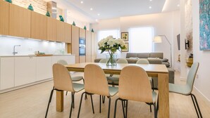 Una cucina moderna con mobili in legno, una zona pranzo con tavolo e sedie, e un soggiorno con divano e lampada.