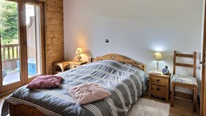 Een slaapkamer met een groot bed, een houten hoofdbord, een nachtkastje met een lamp, een stoel en een schuifdeur naar een buitenruimte.