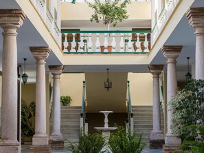 Un patio con columnas, una fuente y un balcón con un árbol.