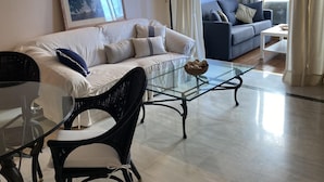 A modern living room with a sofa, a glass coffee table, and a wicker chair.