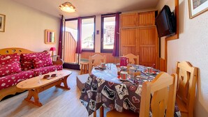 A cozy room with a wooden sofa, a dining table with a patterned tablecloth, and a television mounted on the wall.