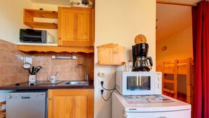 A compact kitchen with wooden cabinets, a microwave, a coffee maker, and a dishwasher.