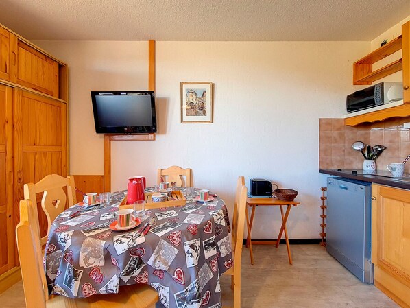 A compact kitchen with wooden cabinets, a microwave, and a small dining table with a patterned tablecloth. - Cozy studio at the foot of the slopes with balcony (Les Menuires)