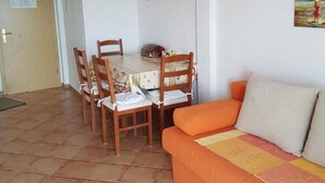 A living room with a dining table and chairs, a sofa, and a door. - Apartments Jereb (Podgora)
