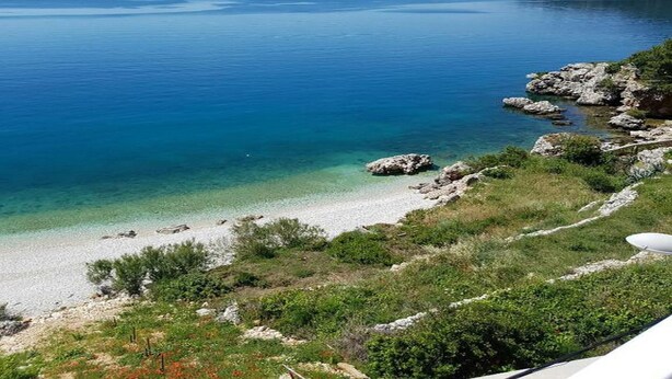 A coastal landscape with clear blue waters, a sandy beach, and rocky outcrops. - Apartments Jereb (Podgora)