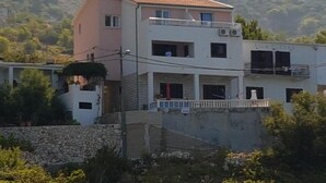 A two-story building with a balcony, a stone wall in the foreground, and a mountainous backdrop. - Apartments Jereb (Podgora)