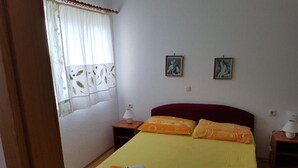A bedroom with a bed, two bedside tables, a window with curtains, and two wall-mounted pictures. - Apartments Jereb (Podgora)