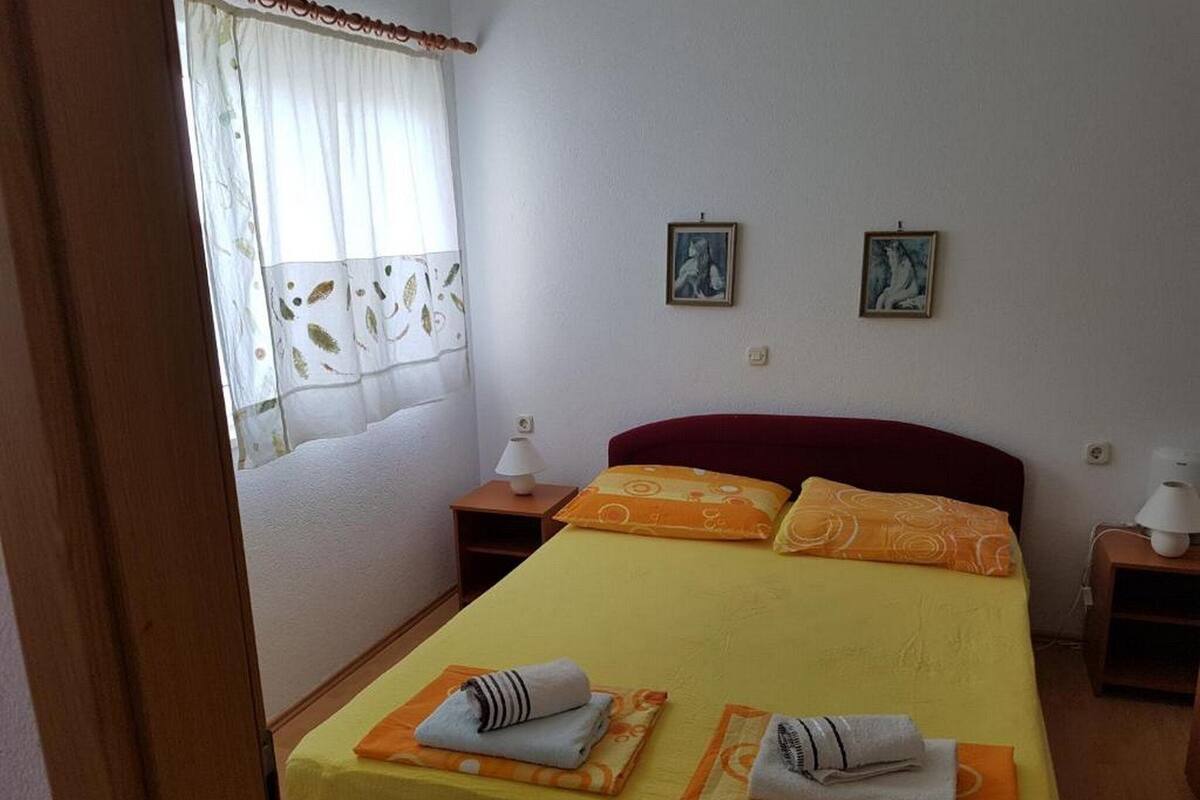 A bedroom with a bed, two bedside tables, a window with curtains, and two wall-mounted pictures.